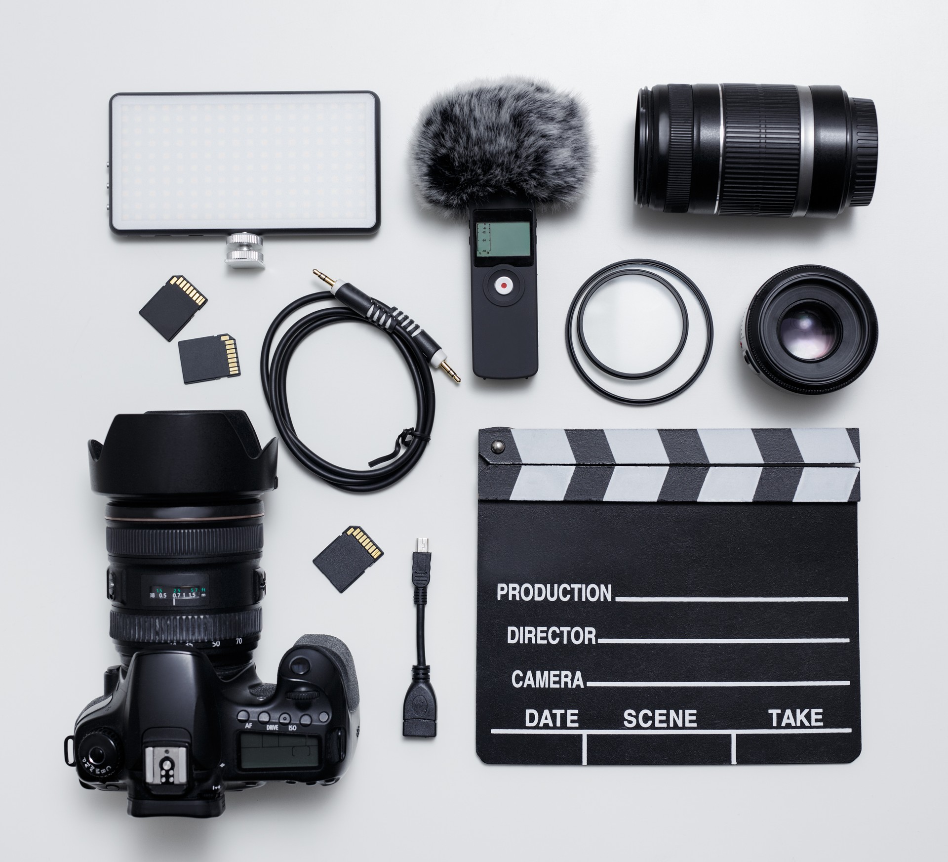 vidéographie et équipement de photographie - vue supérieure plat pose de l’appareil photo moderne dslr, lentilles, filtres, microphone avec pare-brise, lumière led, cartes mémoire et panneau clapper sur la table blanche